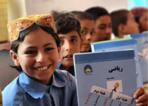 Afghan children smiling and holding textbooks at a Gate of Hope education program in Afghanistan