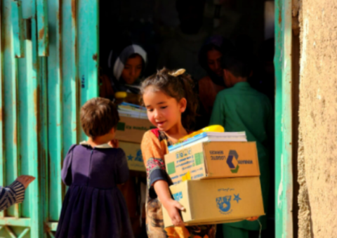 Young Afghan girl carrying aid boxes during Gate of Hope kit distribution program in Afghanistan